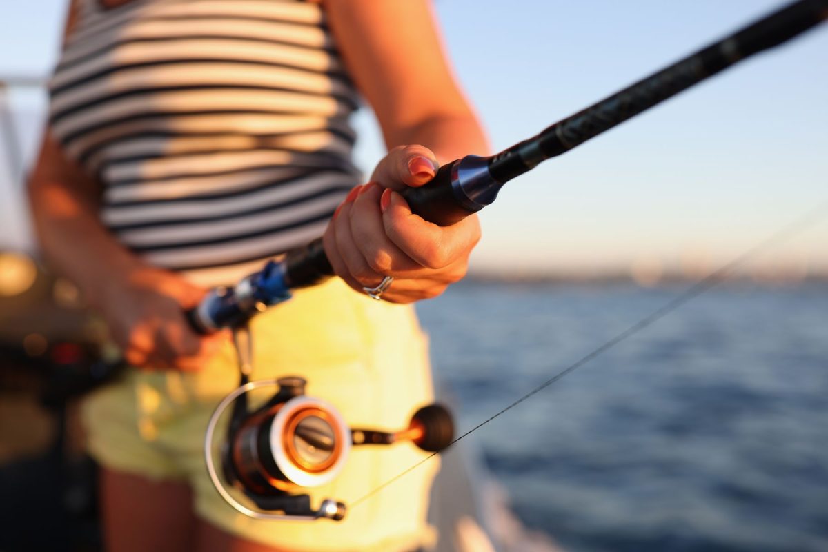 Close-up of a woman holding a saltwater fishing rod on a boat at sunset, showcasing premier sportfishing and charter excursions available on the Forgotten Coast.
